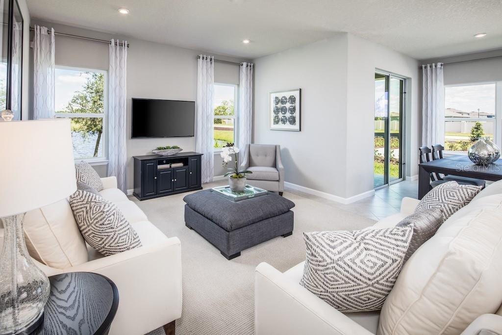 A living room features white sofas, a dark gray ottoman, a television, and dining area — 1079 OCEAN LODGE ROAD, LADY LAKE, FL