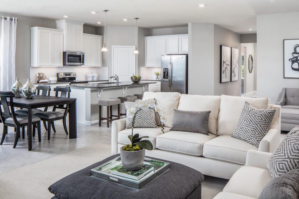 An open-concept living room and kitchen featuring white cabinetry, stainless appliances, and neutral furniture — 1079 OCEAN LODGE ROAD, LADY LAKE, FL