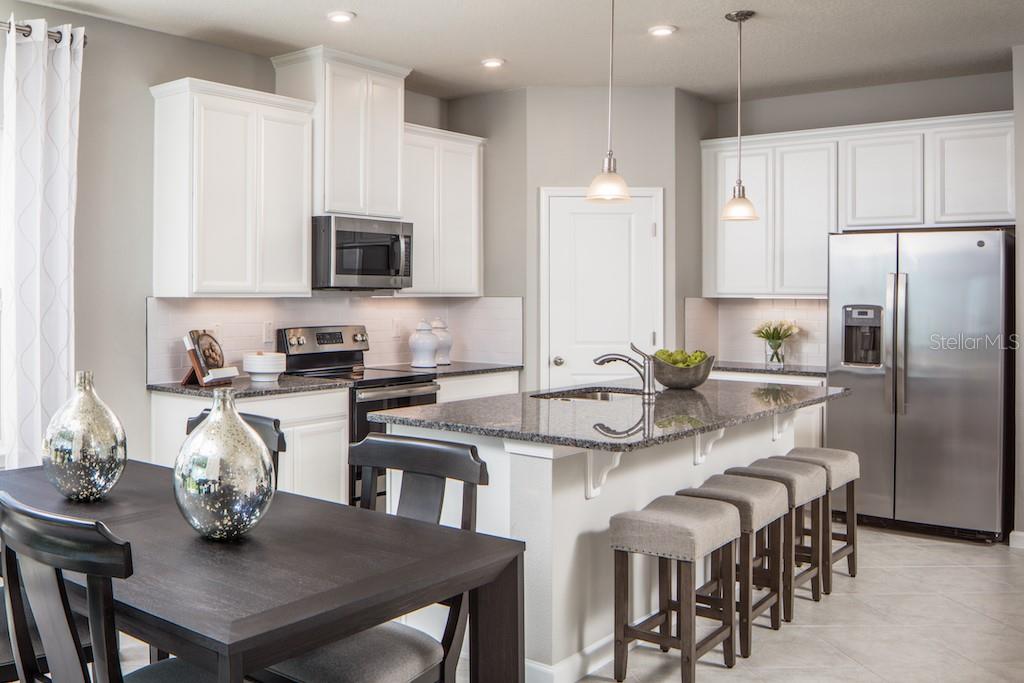 A kitchen with white cabinets, granite countertops, stainless steel appliances, and a dining table — 1079 OCEAN LODGE ROAD, LADY LAKE, FL