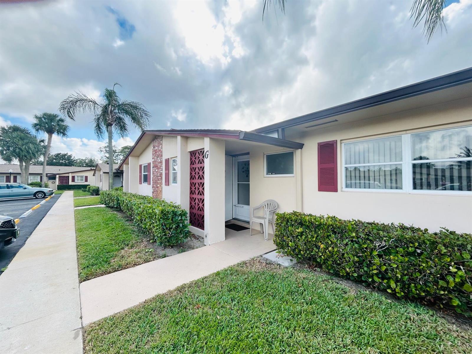 A single-story residential building features a beige exterior, red shutters, and a decorative screen wall — 2990 Crosley Drive E # G, West Palm Beach FL 33415, WEST PALM BEACH, FL
