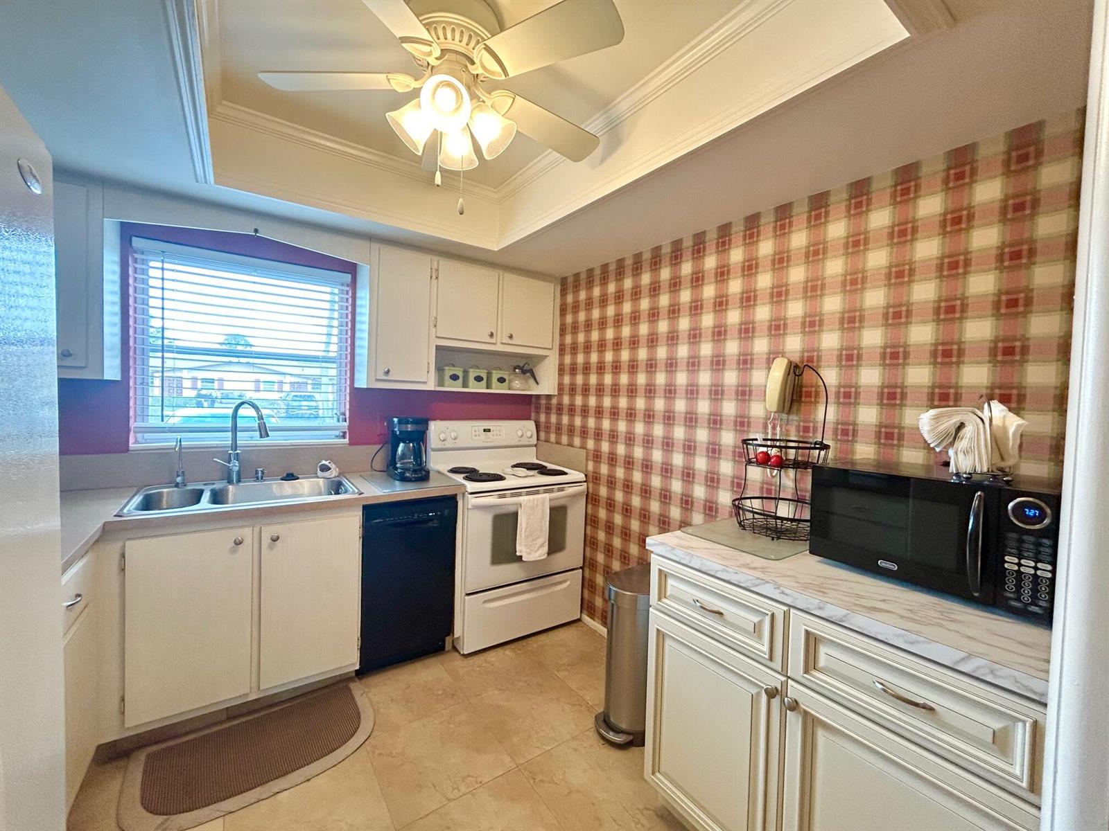 A kitchen features white cabinets, a plaid wallpaper accent wall, and a ceiling fan — 2990 Crosley Drive E # G, West Palm Beach FL 33415, WEST PALM BEACH, FL
