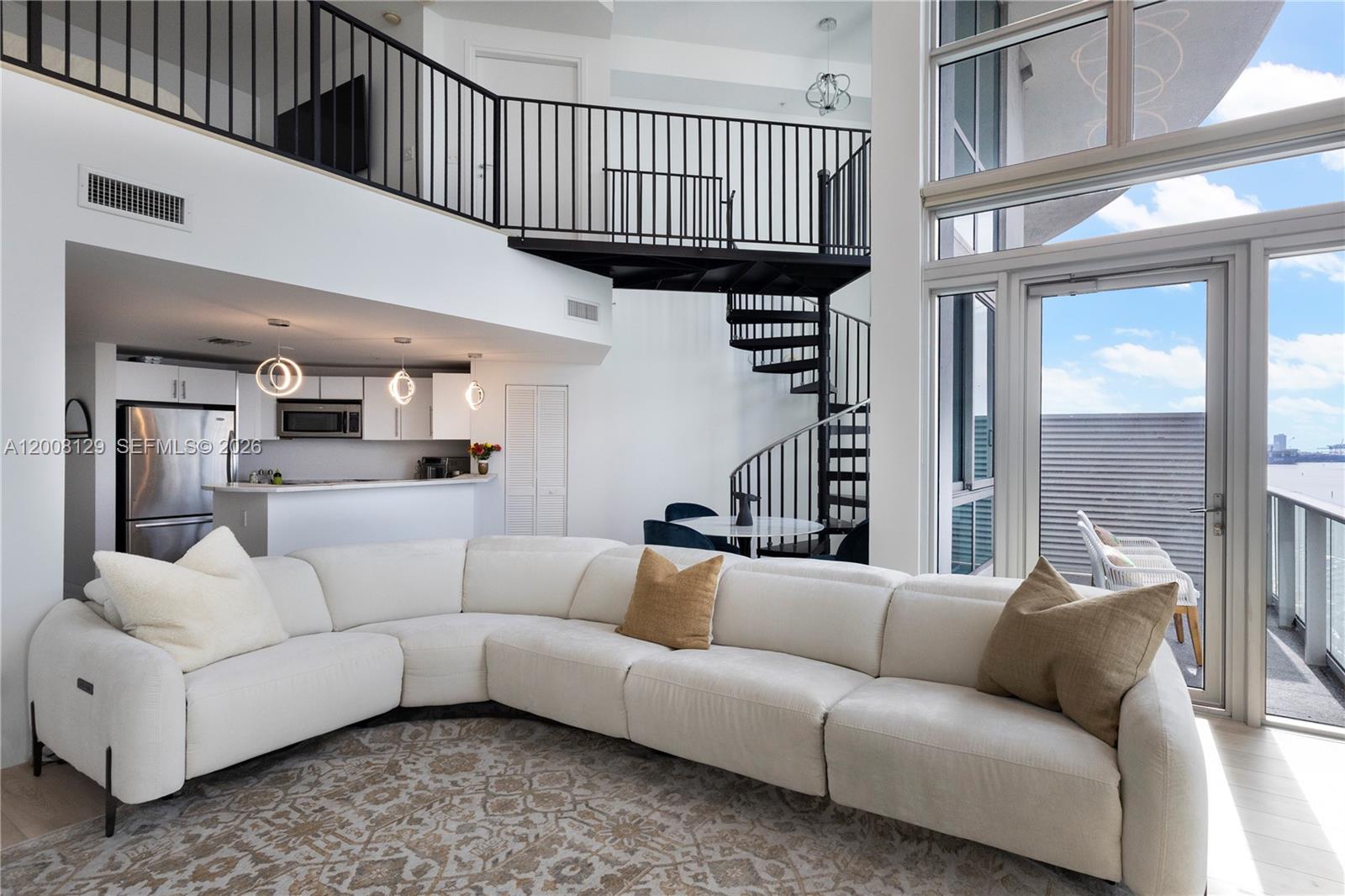 A modern living room features a white sectional sofa, a spiral staircase, and floor-to-ceiling windows — 300 S Biscayne Blvd # 1014, Miami FL 33131, MIAMI, FL