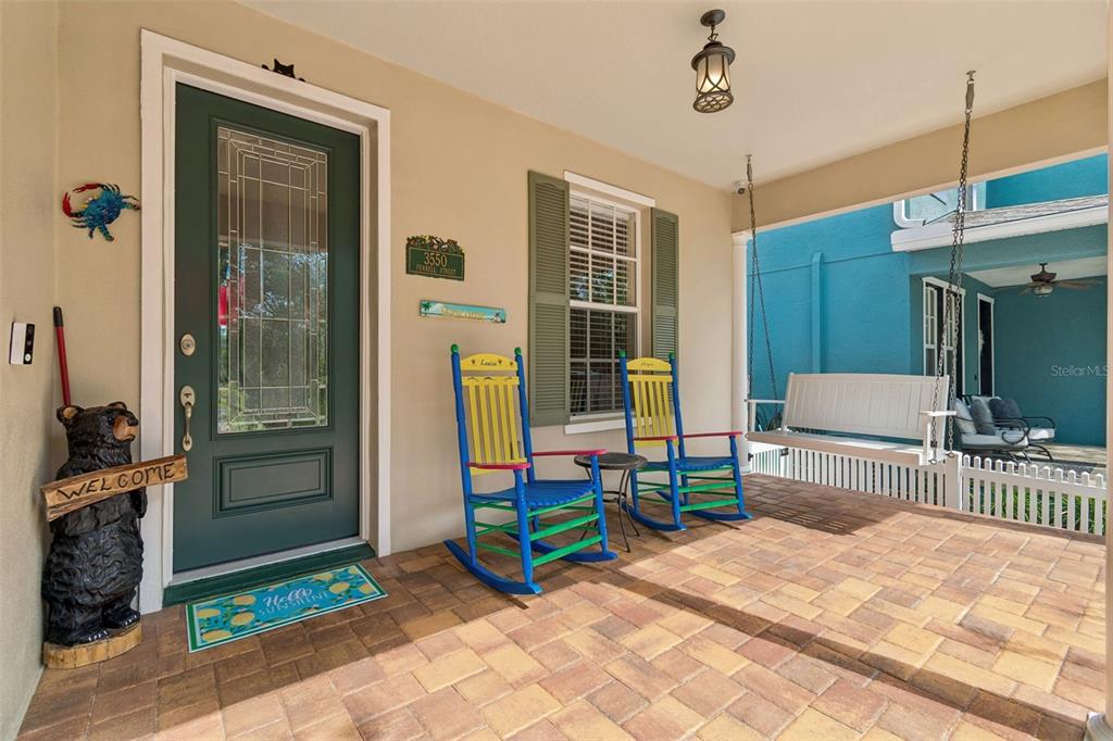 A covered front porch features a green door, two colorful rocking chairs, and a hanging bench — 3550 FERRELL STREET, NEW PORT RICHEY, FL