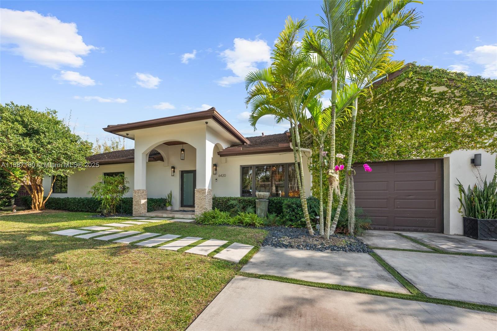 A single-story house features a covered entryway, a brown garage door, and palm trees — 6420 SW 63rd Ter, South Miami FL 33143, SOUTH MIAMI, FL