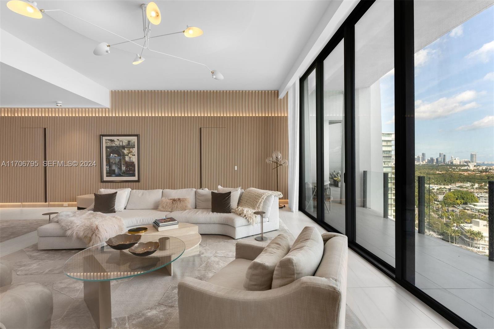 A modern living room features wood-slat walls, a curved sectional sofa, and floor-to-ceiling windows — 2811 S Bayshore Dr, Miami FL 33133, MIAMI, FL