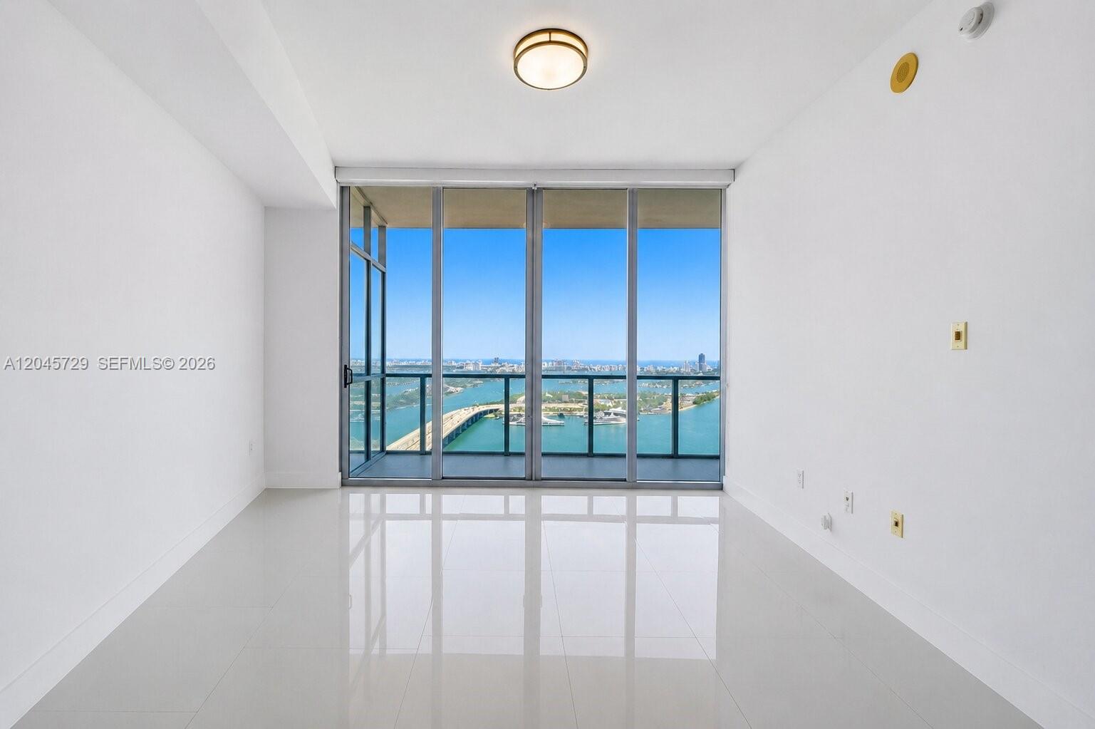 An empty room with white tile floors features floor-to-ceiling windows overlooking a bay — 1100 Biscayne Blvd # 4402, Miami FL 33132, MIAMI, FL