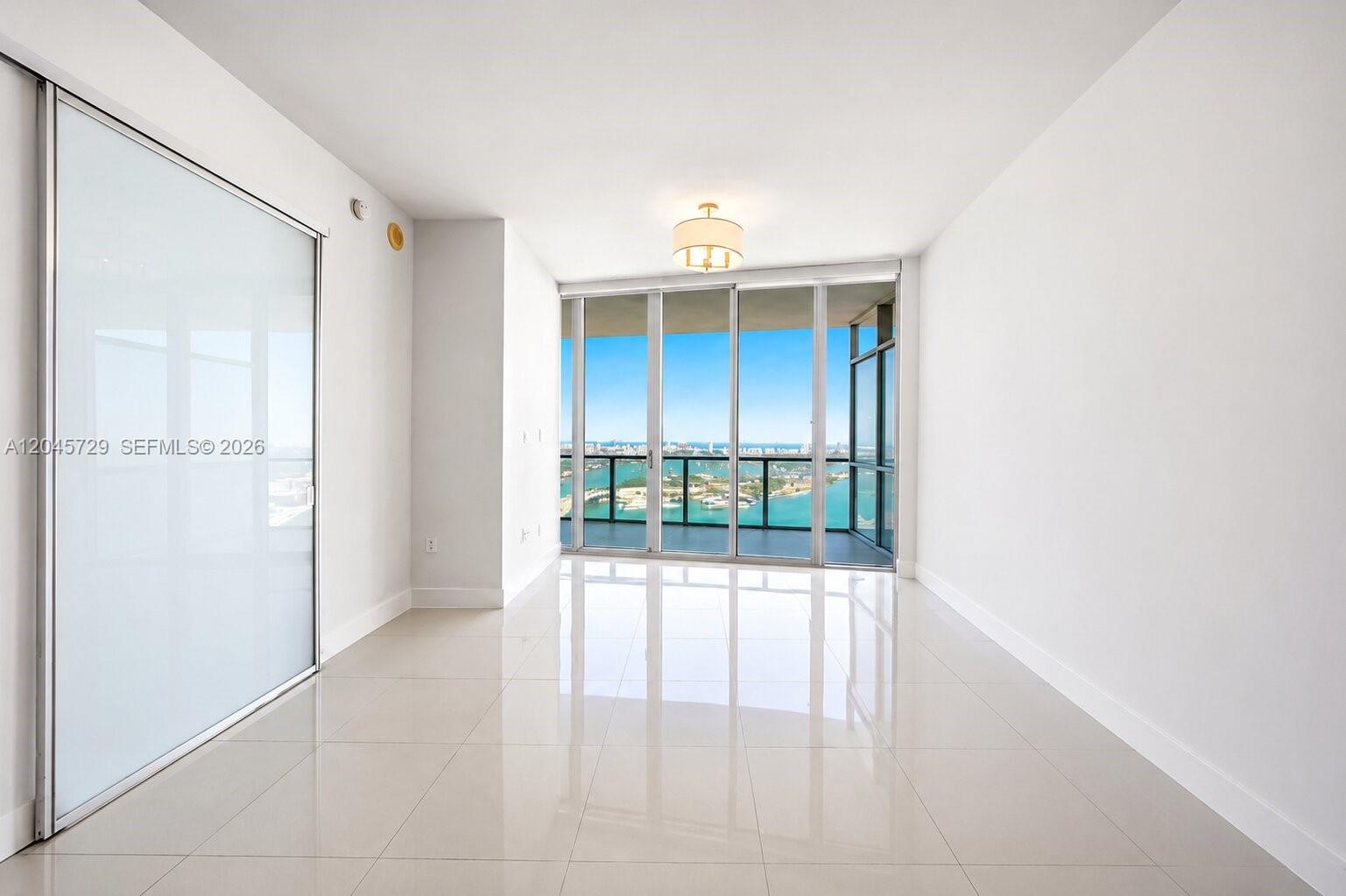 An empty room with white walls, tiled floors, and floor-to-ceiling windows overlooking the water — 1100 Biscayne Blvd # 4402, Miami FL 33132, MIAMI, FL