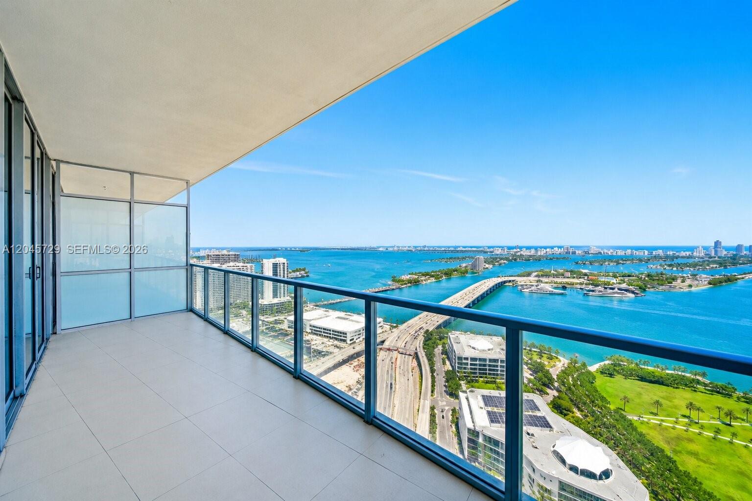 A high-rise balcony features glass railings overlooking a bridge, a bay, and a city park — 1100 Biscayne Blvd # 4402, Miami FL 33132, MIAMI, FL