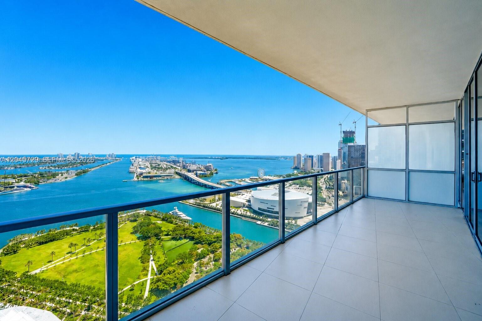 A high-rise balcony with glass railings overlooks a park, a bay, and a city skyline — 1100 Biscayne Blvd # 4402, Miami FL 33132, MIAMI, FL