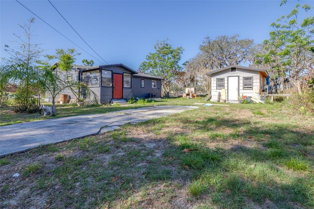 A gray house with a red door and a detached shed sit on a grassy lot — 3726 KENILWORTH BOULEVARD, SEBRING, FL