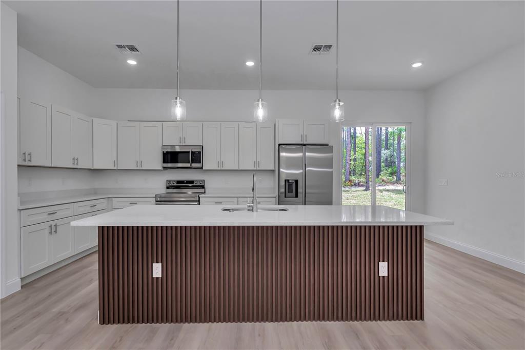 A modern kitchen features white cabinetry, a large island with wood-slat detailing, and stainless appliances — 7565 N SANTOS DRIVE, CITRUS SPRINGS, FL