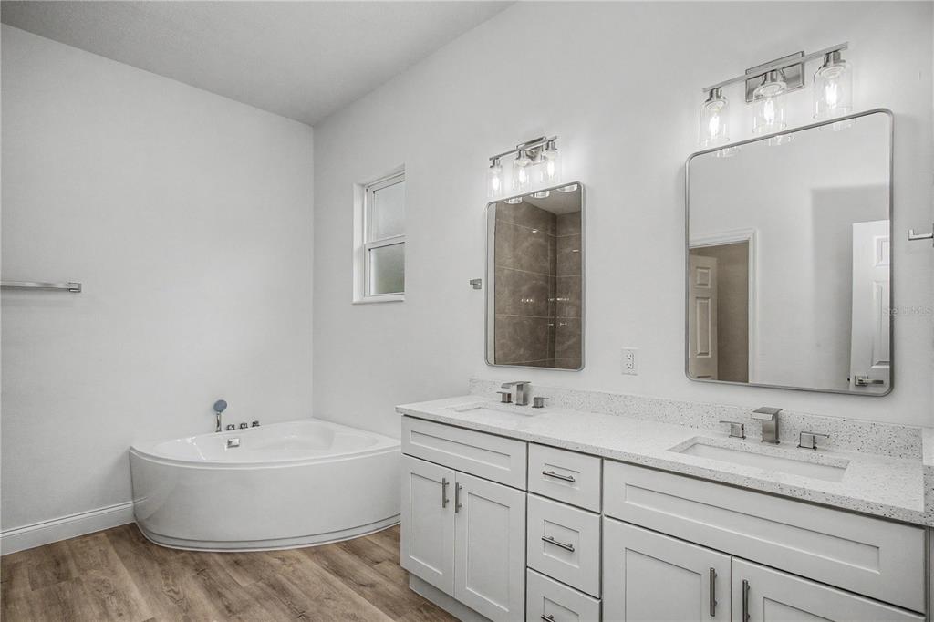 A bathroom with a white double vanity, quartz countertops, two mirrors, and a corner tub — 7565 N SANTOS DRIVE, CITRUS SPRINGS, FL