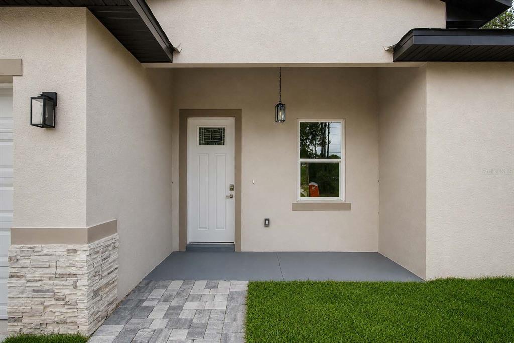 The exterior of a house features a covered entryway with a white door and stone accents — 7565 N SANTOS DRIVE, CITRUS SPRINGS, FL