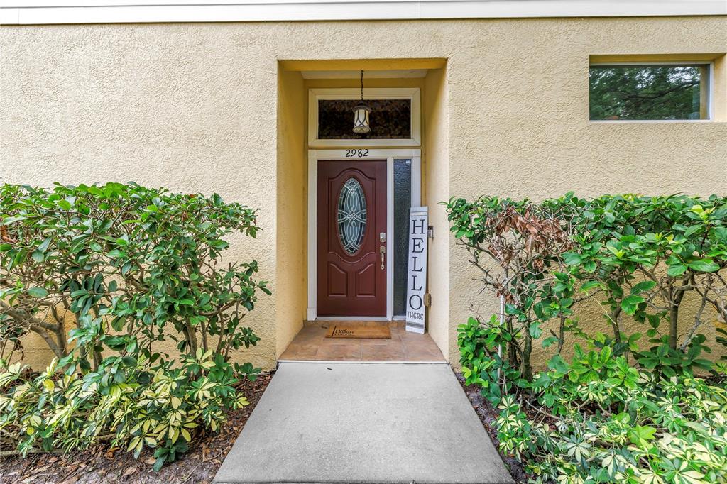 A screened-in porch features lime green chairs, a patterned rug, and a view of trees — 2982 ESTANCIA PLACE, CLEARWATER, FL