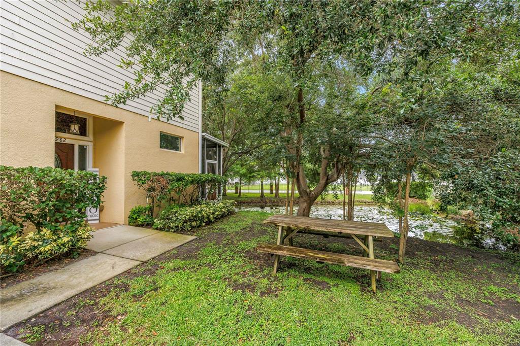 A wooden picnic table sits on a grassy lawn beside a pond near a building — 2982 ESTANCIA PLACE, CLEARWATER, FL