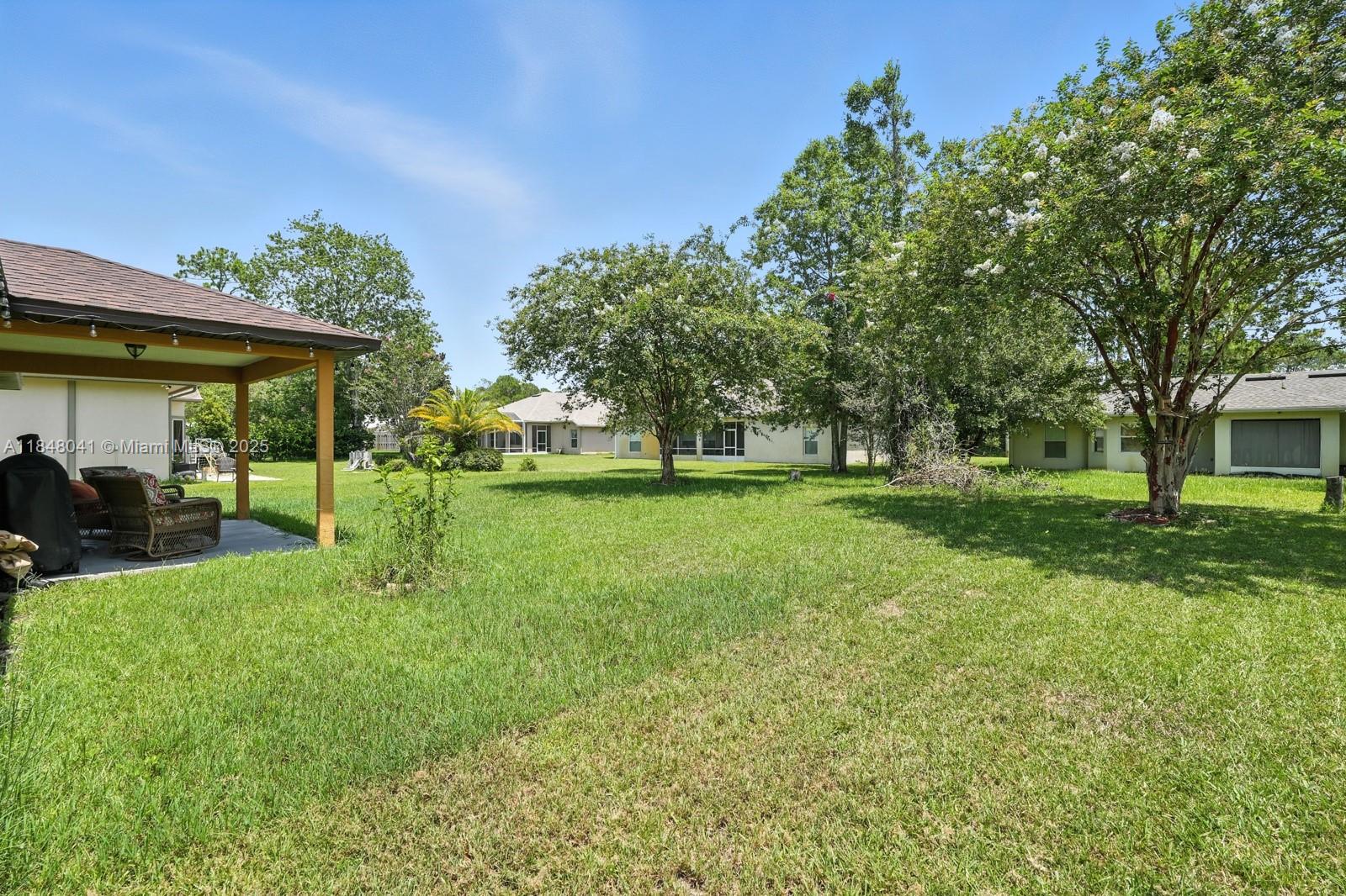 A grassy backyard features a covered patio with outdoor furniture and several mature trees — 20 Bennett Lane, Palm Coast FL 32137, PALM COAST, FL