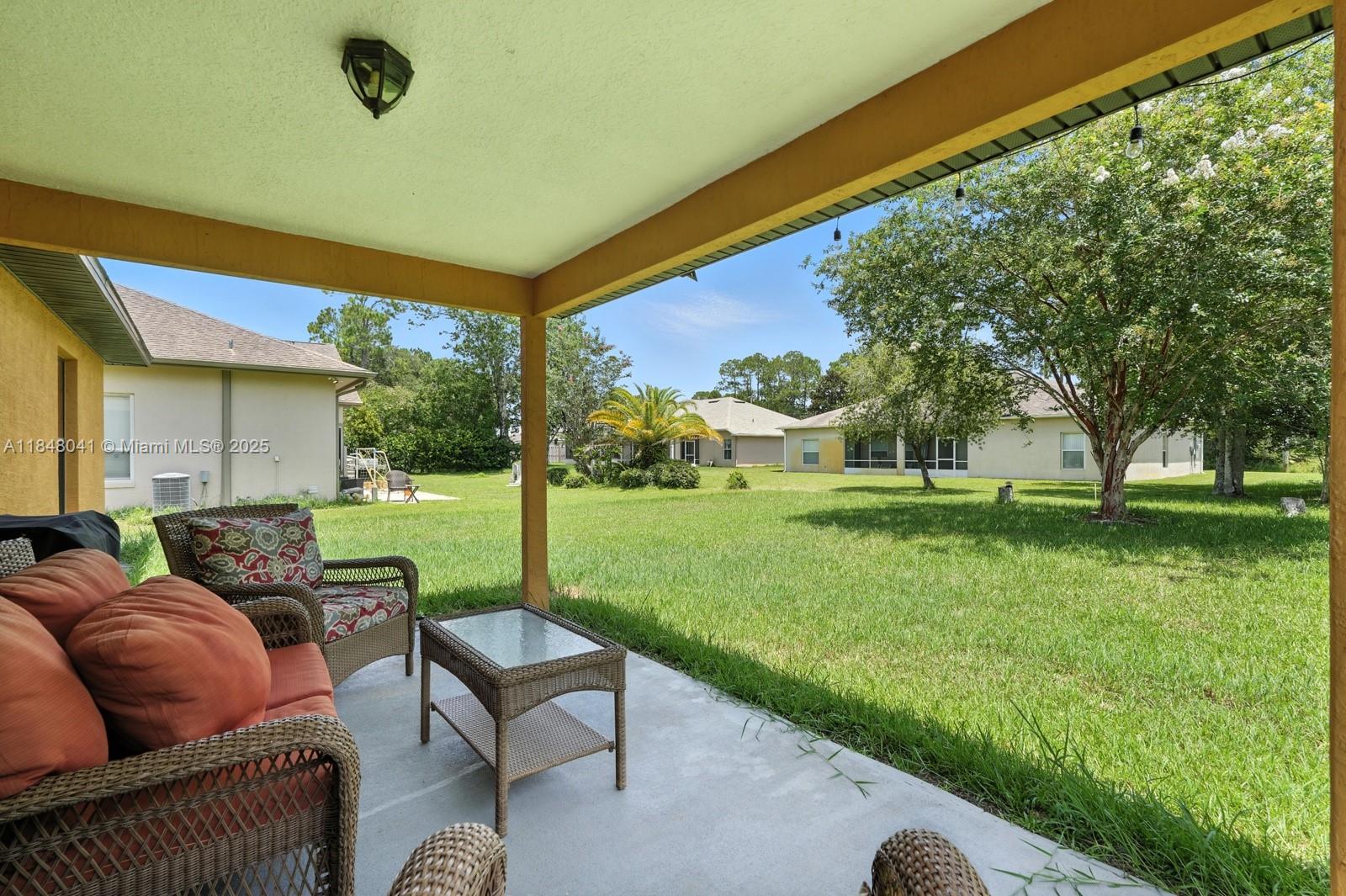 A covered patio with wicker furniture overlooks a grassy backyard and neighboring houses — 20 Bennett Lane, Palm Coast FL 32137, PALM COAST, FL