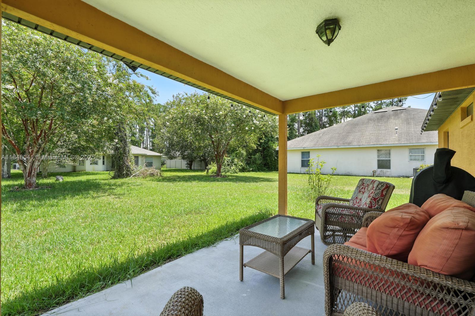 A covered concrete patio features wicker furniture overlooking a grassy backyard with trees — 20 Bennett Lane, Palm Coast FL 32137, PALM COAST, FL