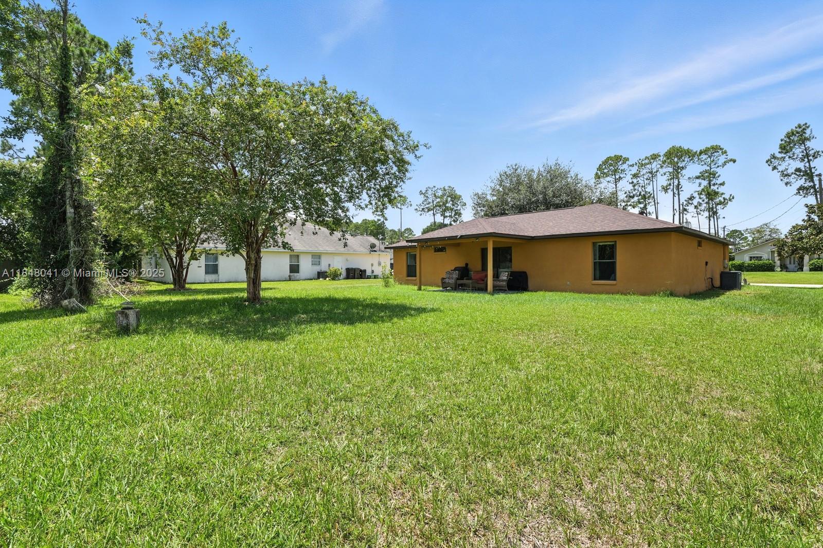A yellow house with a covered patio sits on a large, grassy lot — 20 Bennett Lane, Palm Coast FL 32137, PALM COAST, FL