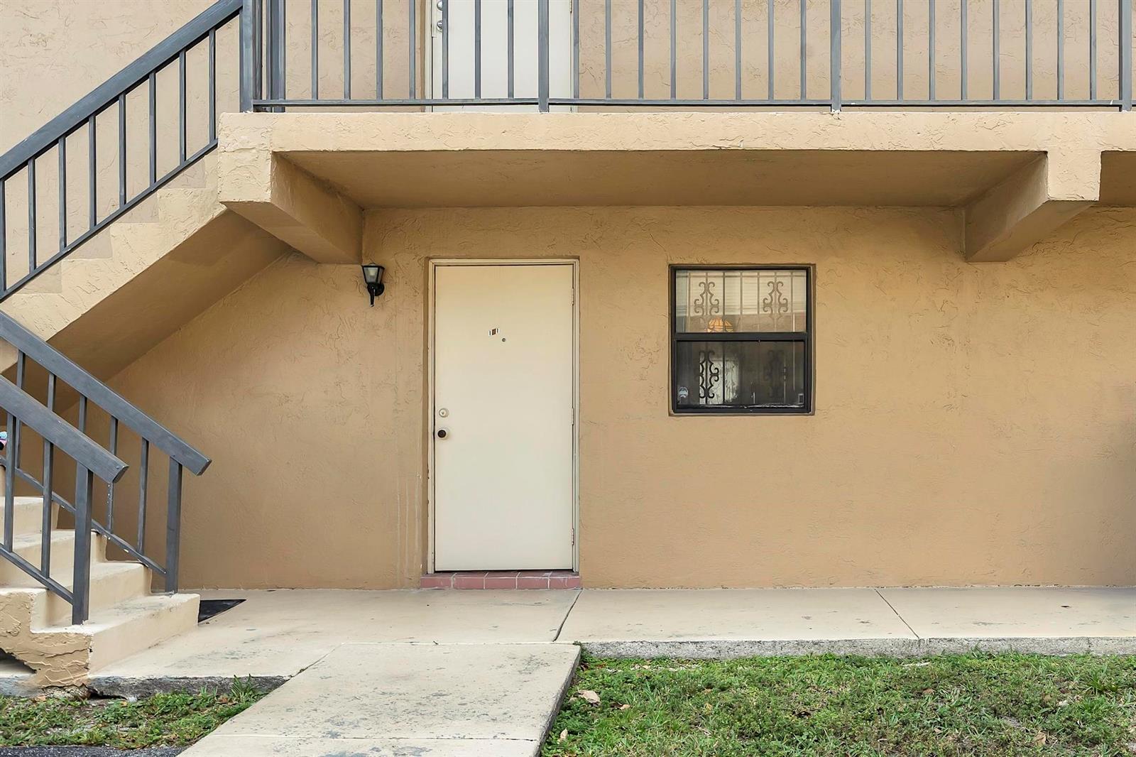 A beige exterior wall features a single door, a window with security bars, and stairs — 6715 W 26th Drive # 6, Hialeah FL 33016, HIALEAH, FL