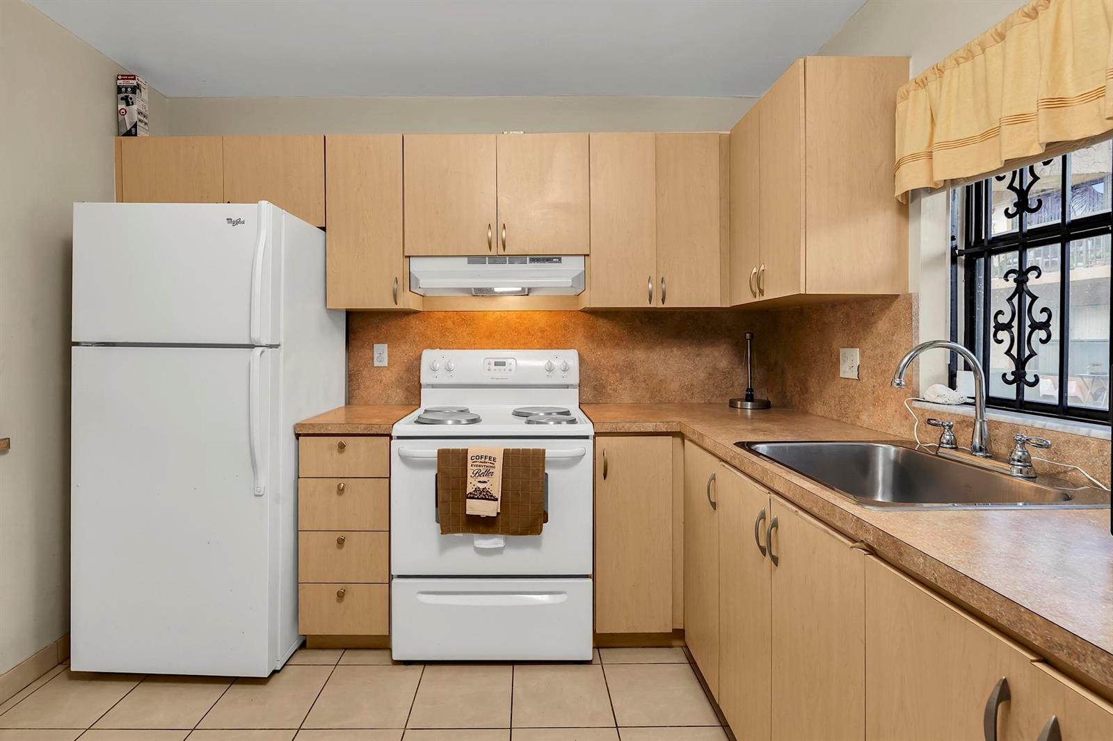 A kitchen with light wood cabinets, white appliances, a laminate countertop, and a window with bars — 6715 W 26th Drive # 6, Hialeah FL 33016, HIALEAH, FL
