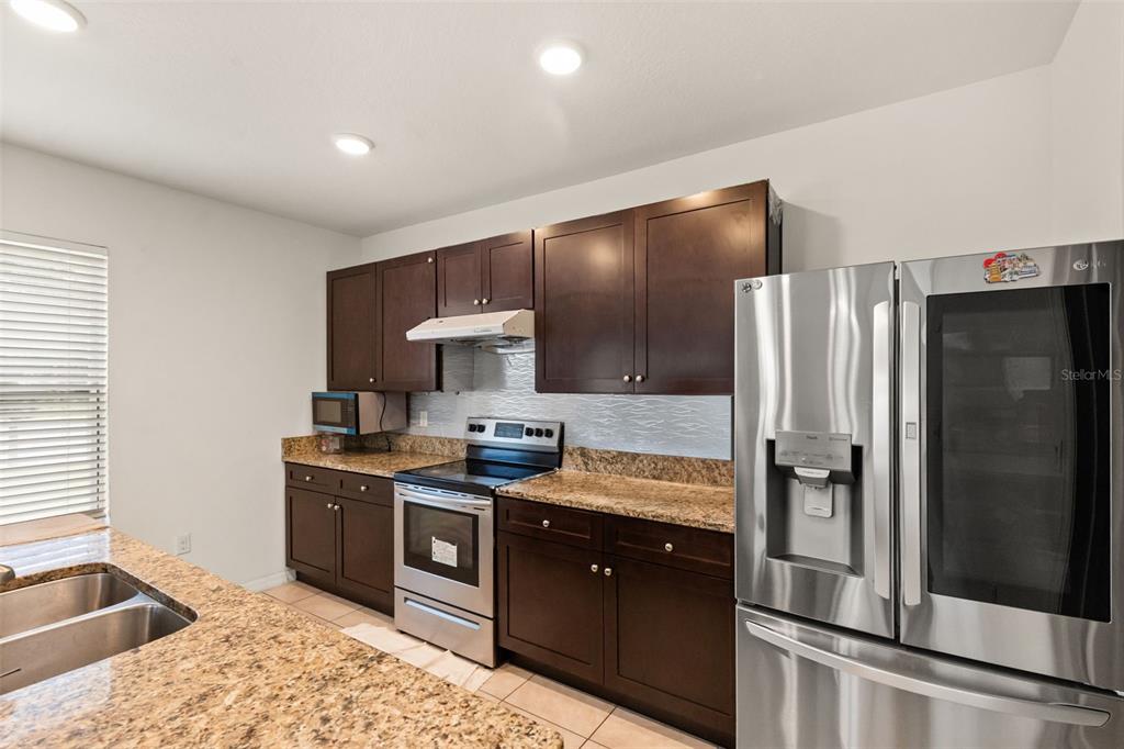 A kitchen features dark wood cabinets, granite countertops, and stainless steel appliances — 166 ST THOMAS DR, MULBERRY, FL
