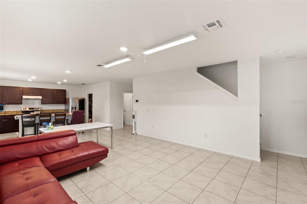 A living room with a red sectional sofa, tile flooring, and an adjacent kitchen area — 166 ST THOMAS DR, MULBERRY, FL