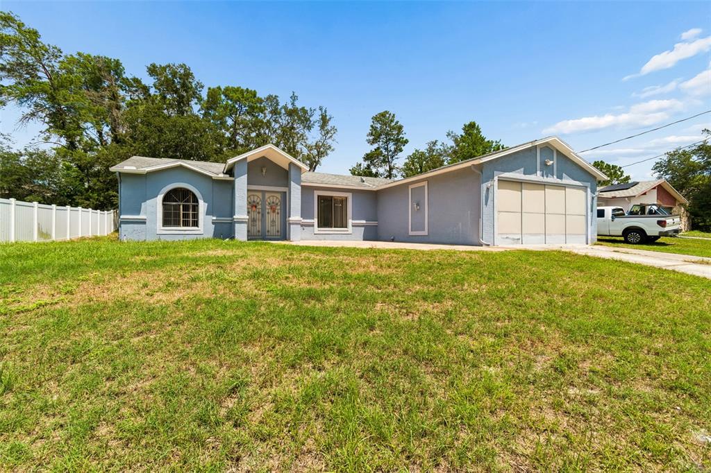 A light blue single-story house with a two-car garage and a front lawn at dusk — 4235 CASTLE AVENUE, SPRING HILL, FL