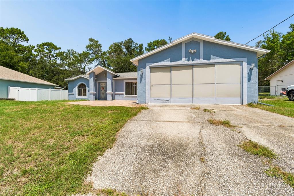 A single-story blue house with a front-facing garage and a white vinyl fence — 4235 CASTLE AVENUE, SPRING HILL, FL