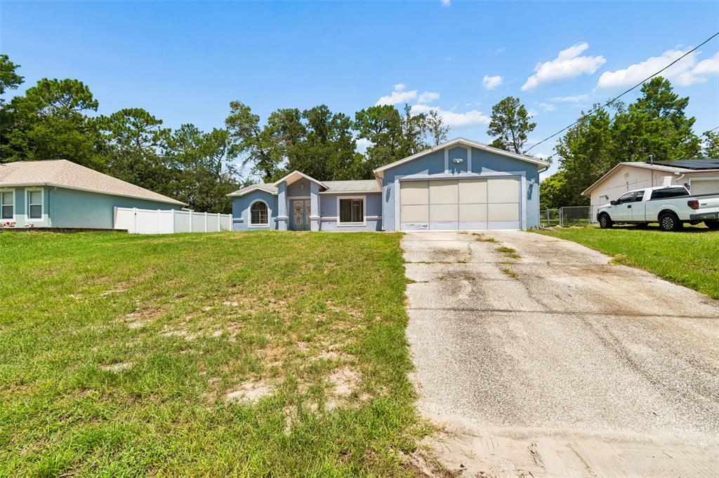 A light blue single-story house features a paved driveway, arched window, and double front doors — 4235 CASTLE AVENUE, SPRING HILL, FL