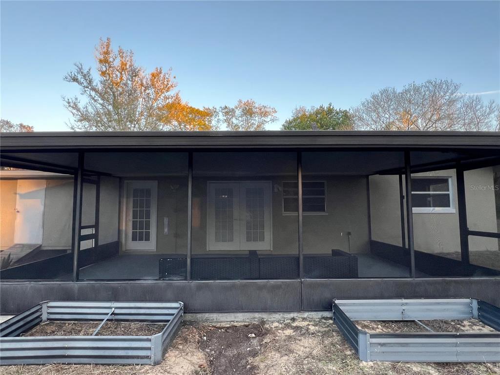 A screened-in patio features two metal garden beds in the foreground and exterior house doors — 4850 N LADYBUG DRIVE, CRYSTAL RIVER, FL