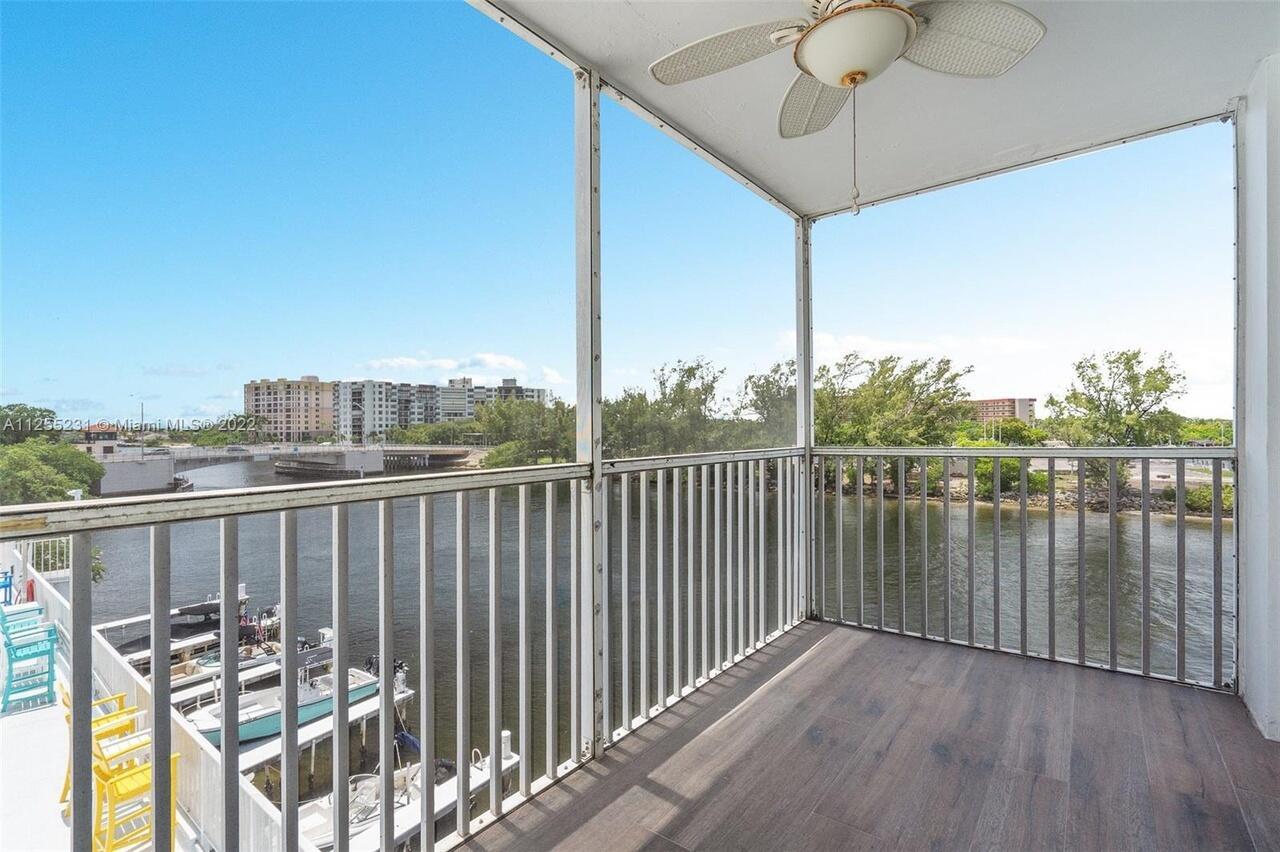 A screened-in balcony with wood-look flooring overlooks a waterway, a bridge, and nearby buildings — 1505 N Riverside Drive # 404, Pompano Beach FL 33062, POMPANO BEACH, FL