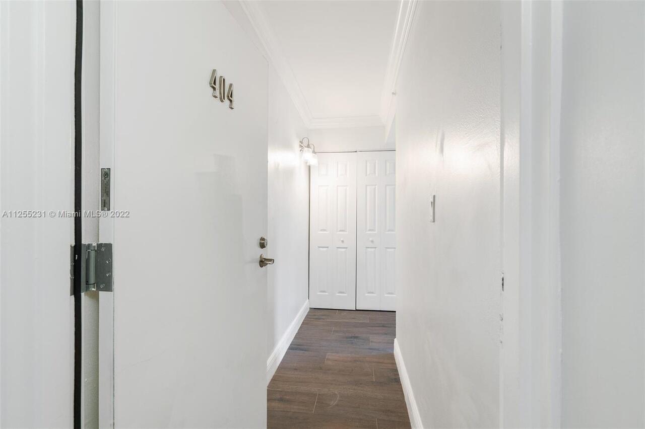 A white hallway features a door labeled 404, wood-look flooring, and a double-door closet — 1505 N Riverside Drive # 404, Pompano Beach FL 33062, POMPANO BEACH, FL