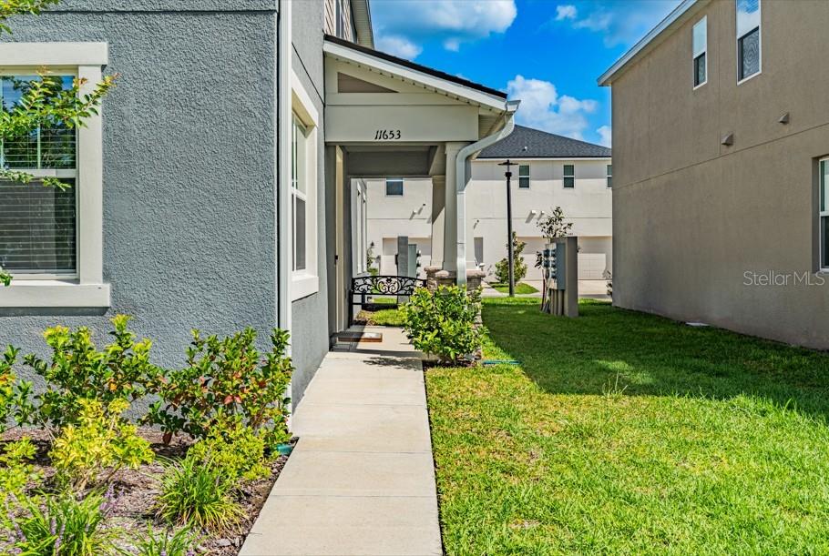 A concrete walkway leads to the covered front entrance of a gray stucco house — 11653 STRAITS WAY, ORLANDO, FL