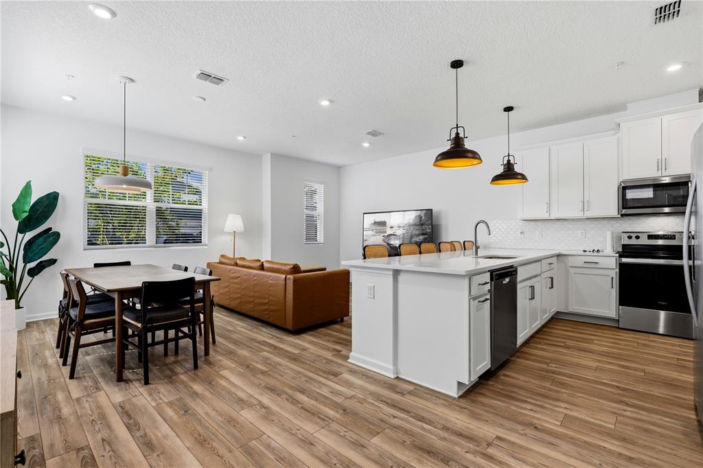 An open-concept kitchen and dining area features white cabinetry, a central island, and wood-look flooring — 11653 STRAITS WAY, ORLANDO, FL