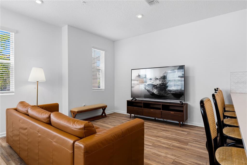 A living room features a brown leather sofa, a television on a stand, and wood-look flooring — 11653 STRAITS WAY, ORLANDO, FL