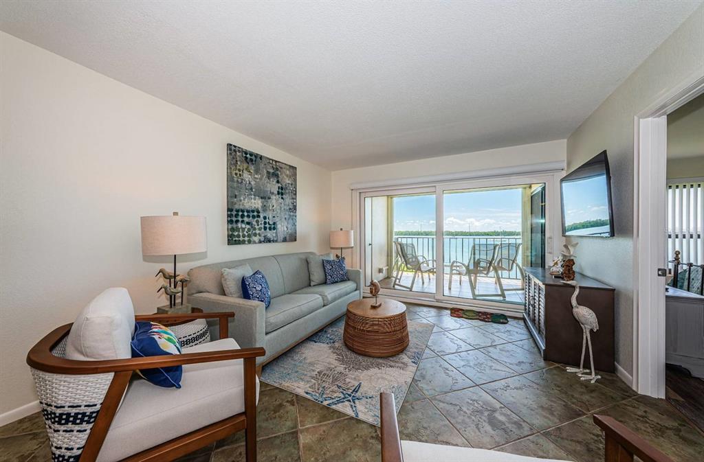 A living room features a sofa, armchairs, tiled floors, and a sliding door to a balcony — 6291 BAHIA DEL MAR CIRCLE UNIT 207, ST PETERSBURG, FL