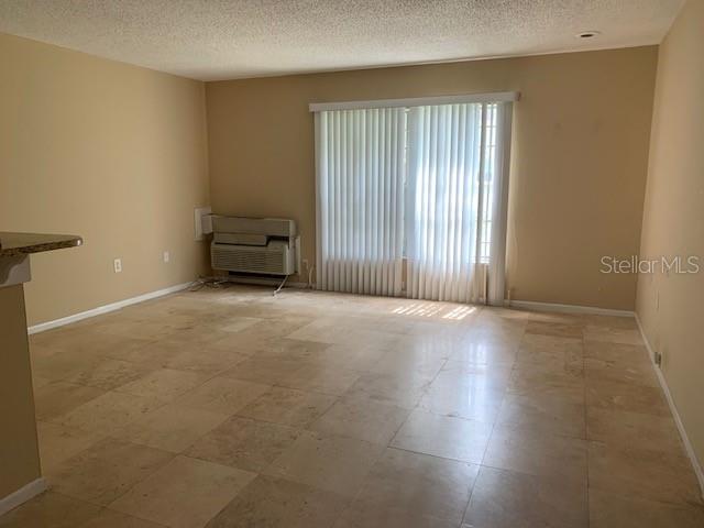 An empty room features light-colored tile flooring, beige walls, and vertical blinds over a window — 120 W AMERICA STREET UNIT 7, ORLANDO, FL