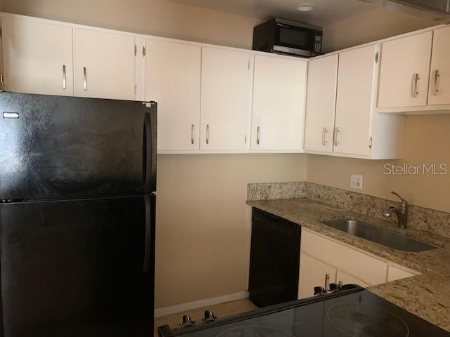 A kitchen features white cabinets, a black refrigerator, a granite countertop, and a stainless sink — 120 W AMERICA STREET UNIT 7, ORLANDO, FL