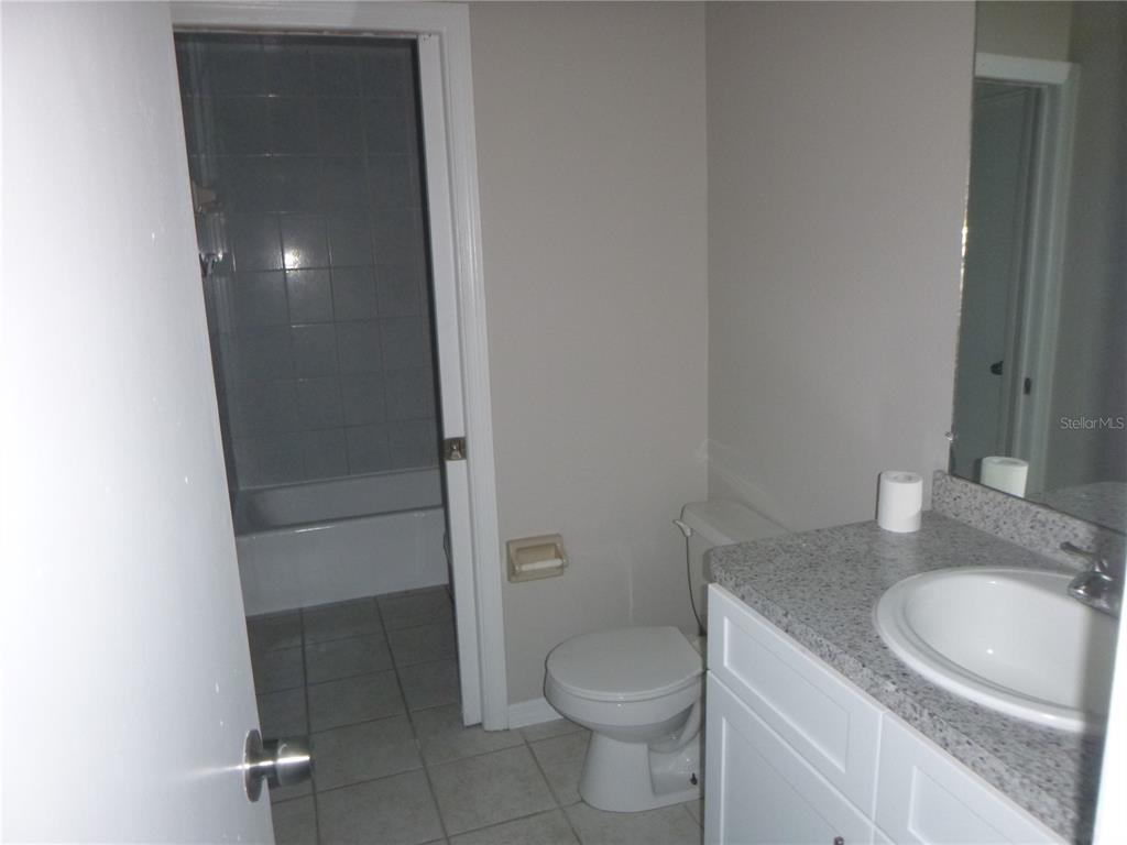 A bathroom features a vanity with a granite countertop, a toilet, and a tiled tub — 4416 HIGHLAND LANE, LAKELAND, FL