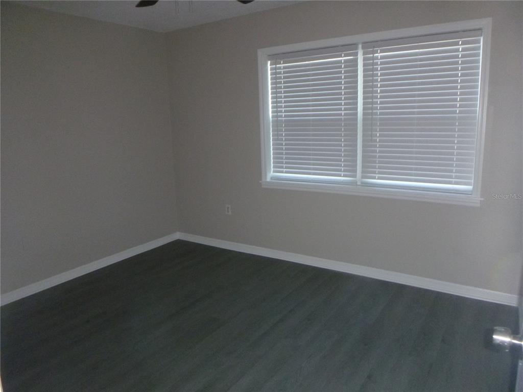 An empty bedroom features gray walls, dark wood-look flooring, and a window with white blinds — 4416 HIGHLAND LANE, LAKELAND, FL