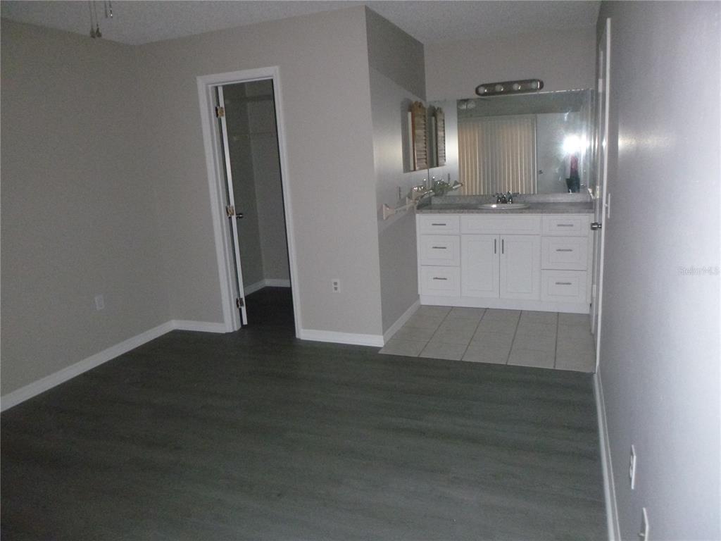 A bedroom features gray flooring, a walk-in closet, and an open vanity area with tile — 4416 HIGHLAND LANE, LAKELAND, FL