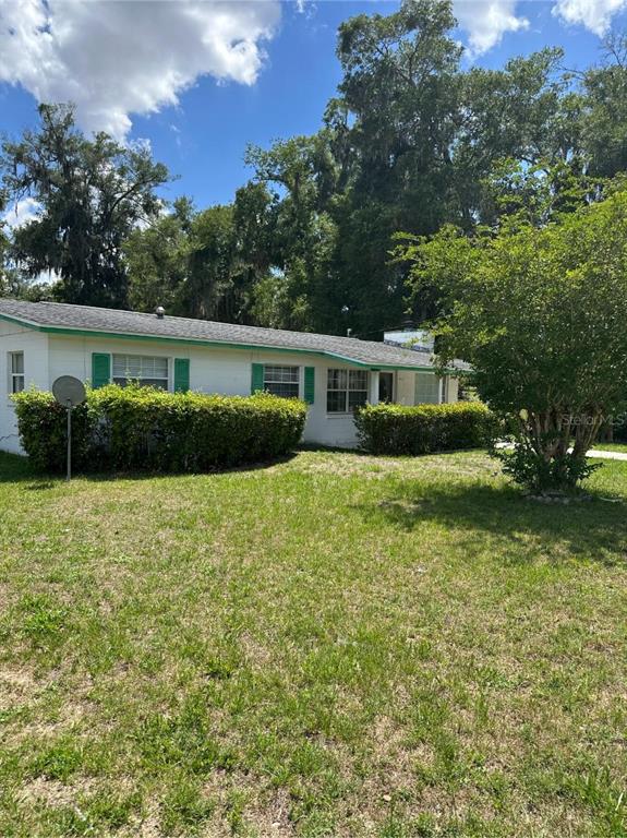 A single-story white house with green shutters and a large front yard under a blue sky — 2602 NW 18TH STREET, OCALA, FL