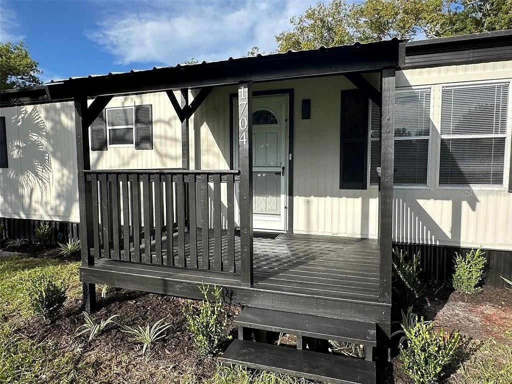 A mobile home features a black wooden porch with stairs and a white front door — 1704 MISSOURI AVENUE, ST CLOUD, FL