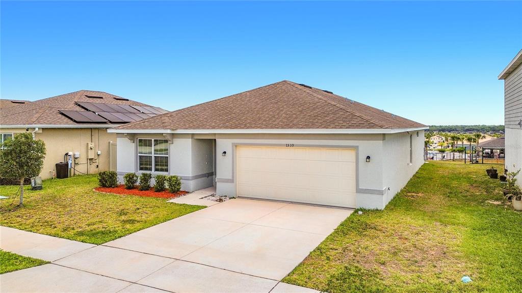 A single-story house with a tan stucco exterior, brown roof, and a two-car garage — 1539 ASPEN AVENUE, DAVENPORT, FL