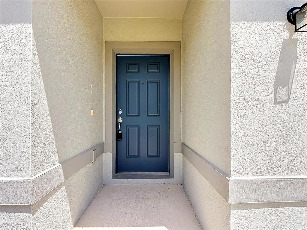 A blue six-panel front door is set within a recessed entryway with stucco walls — 1539 ASPEN AVENUE, DAVENPORT, FL