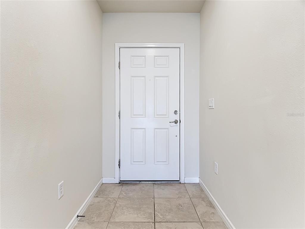 A white front door sits at the end of a narrow entryway with tiled flooring — 1539 ASPEN AVENUE, DAVENPORT, FL