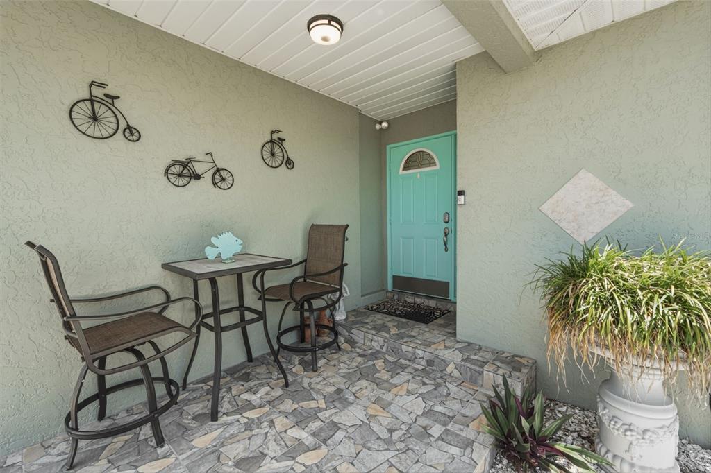 A covered porch features a stone-tiled floor, two chairs, a small table, and a teal door — 200 BELAIRE COURT, PUNTA GORDA, FL