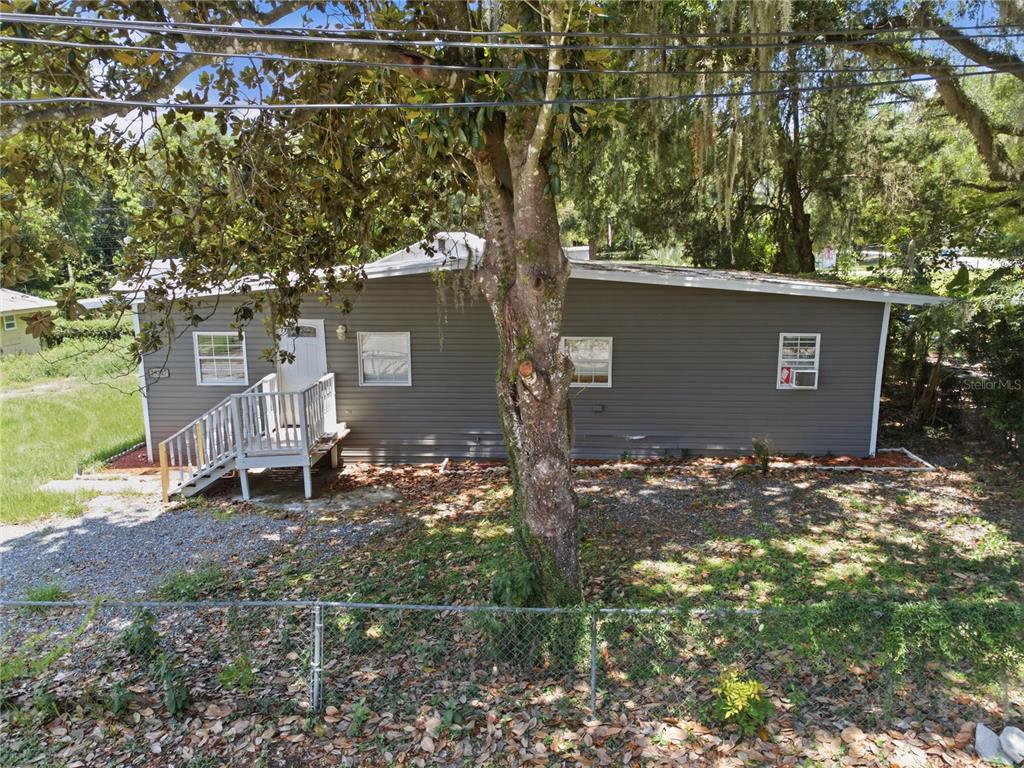 A gray single-story house with a white front porch stands behind a chain-link fence — 39217 FIBELKORN ROAD, ZEPHYRHILLS, FL