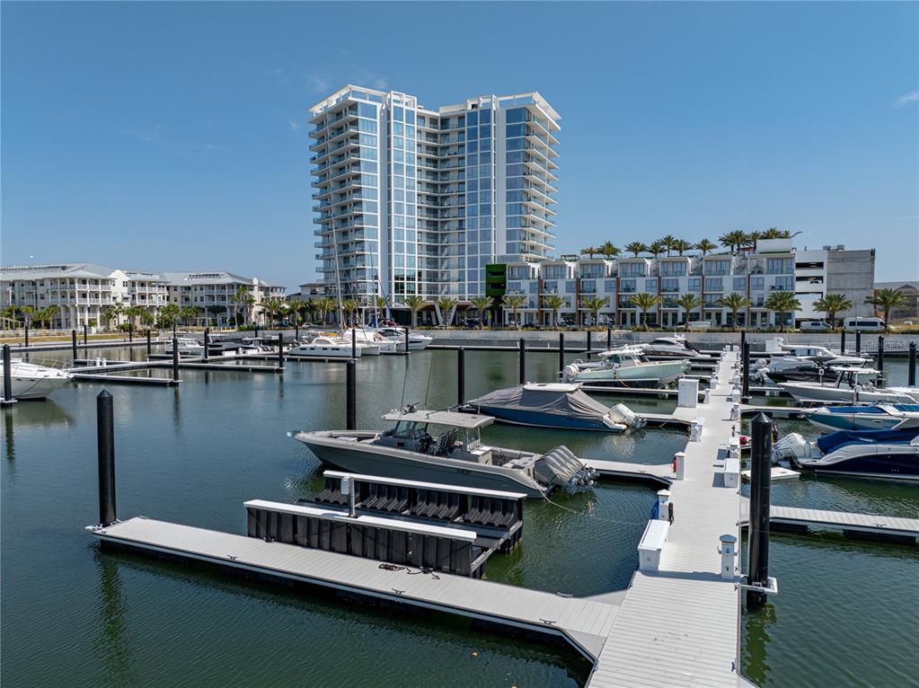 A modern high-rise building overlooks a marina filled with docked boats on a sunny day — 5120 MARINA WAY UNIT D-E-16, TAMPA, FL